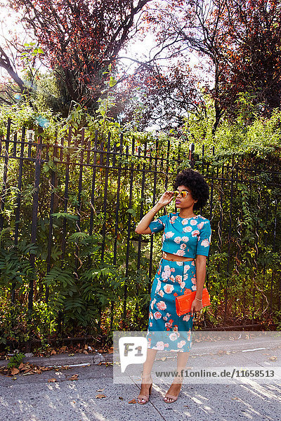 Junge weibliche Mode-Bloggerin mit Afro-Haaren wartet auf dem Bürgersteig eines Parks  New York  USA