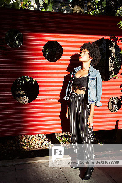 Junge weibliche Mode-Bloggerin mit geschlossenen Augen am sonnenbeschienenen Zaun  New York  USA