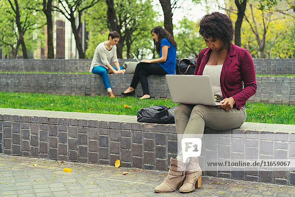 Junge Frau sitzt an der Wand und benutzt einen Laptop