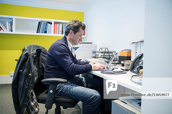 Mann sitzt am Schreibtisch im Büro mit Laptop-Computer