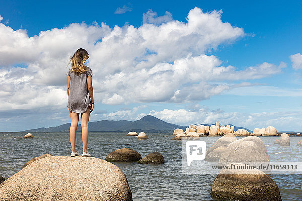 Rückansicht eines jugendlichen Mädchens auf einem Felsen mit Blick auf das Meer