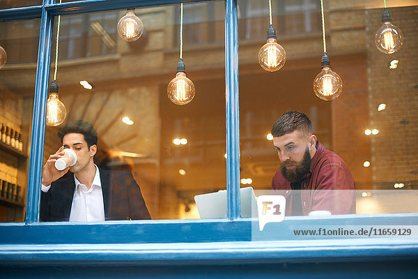 Fensteransicht von Geschäftsleuten  die Kaffee trinken und Laptop im Cafe benutzen