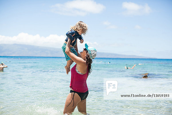 Woman standing in sea  lifting son in air