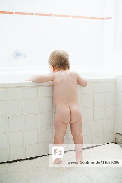 Rear view of naked baby girl peering into bath