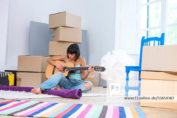 Woman playing guitar surrounded by packing boxes