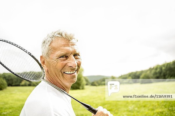 Senior man holding badminton rackets  smiling.