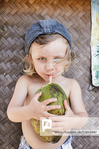 Porträt eines männlichen Kleinkindes mit Baseballmütze  das Kokosmilch trinkt