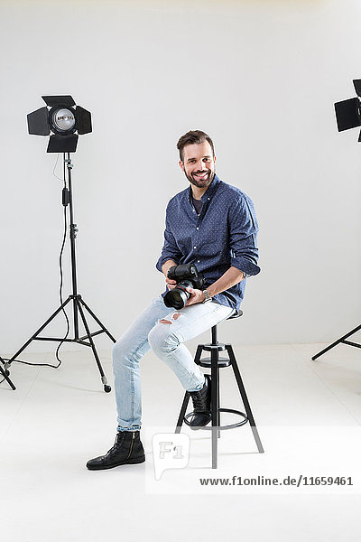 Porträt eines männlichen Fotografen  der auf weißem Hintergrund im Fotografenstudio sitzt