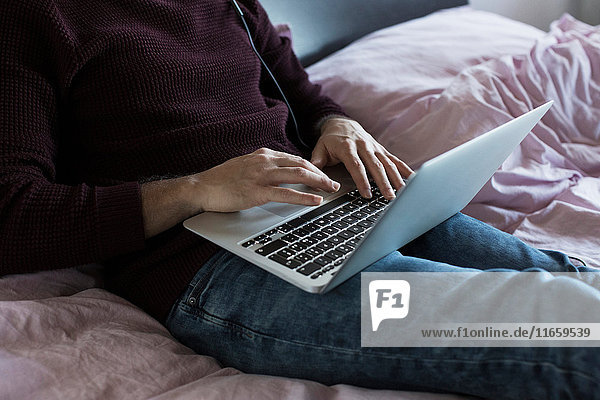 Young man relaxing on bed using laptop mid section