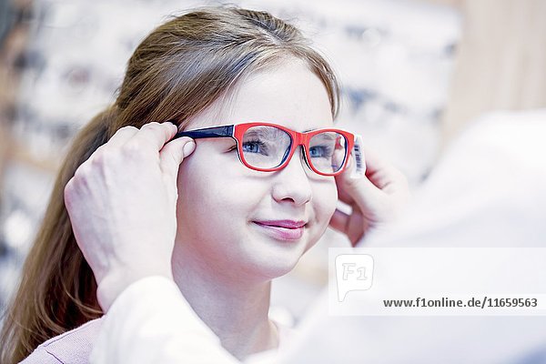 Optiker probiert eine Brille für ein Mädchen in einem Optikerladen an.