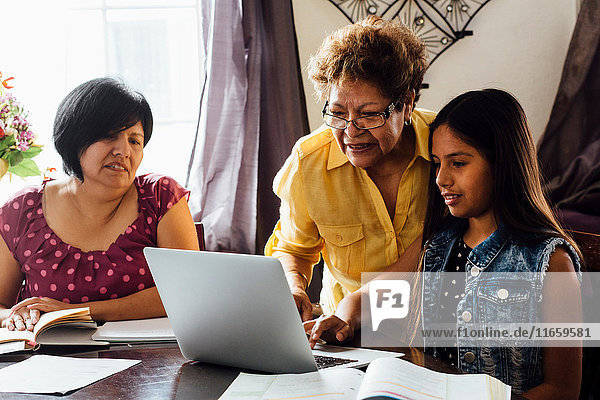 Mutter und Großmutter helfen Mädchen mit dem Laptop bei den Hausaufgaben