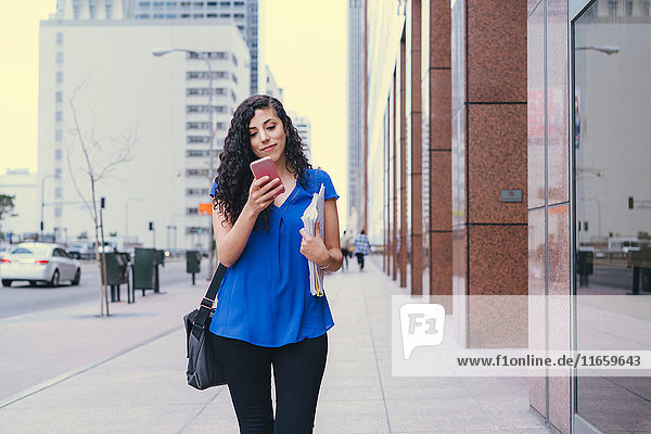 Junge Frau geht auf der Straße und benutzt ein Smartphone