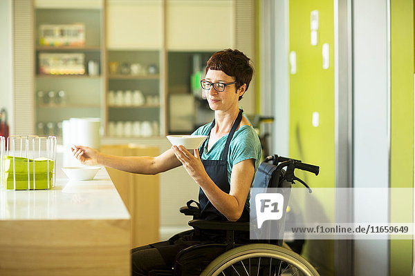 Frau im Rollstuhl  arbeitet im Restaurant  hält Schüssel mit Essen