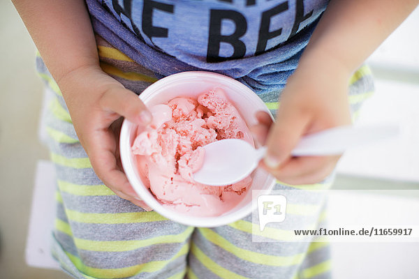 Mittelteil eines Jungen  der eine Schüssel rosa Eiscreme isst