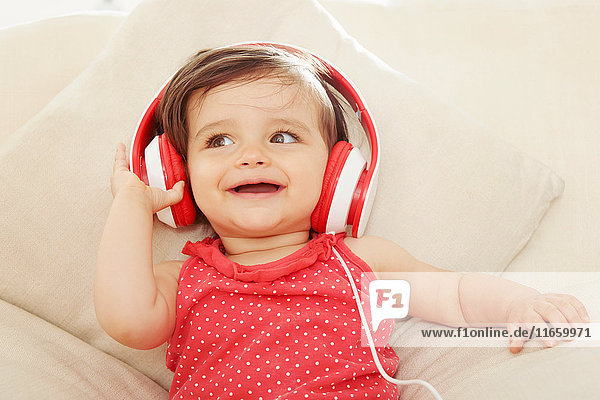 Kleines Mädchen auf dem Sofa hört rote Kopfhörer