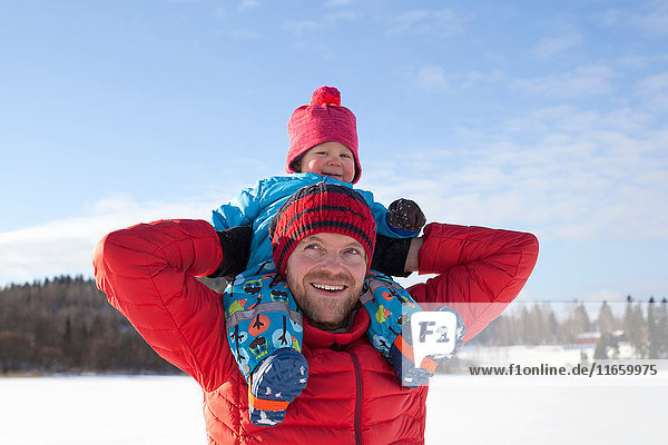 Vater trägt kleinen Sohn auf den Schultern  in schneebedeckter Landschaft
