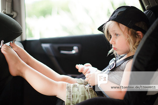 Männliches Kleinkind mit erhobenen Füßen  das auf den Rücksitz eines Autos starrt