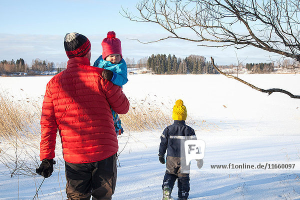 Vater und zwei Söhne spazieren in schneebedeckter Landschaft  Rückansicht