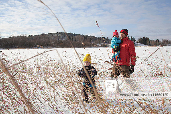 Vater geht mit zwei Söhnen in schneebedeckter Landschaft spazieren