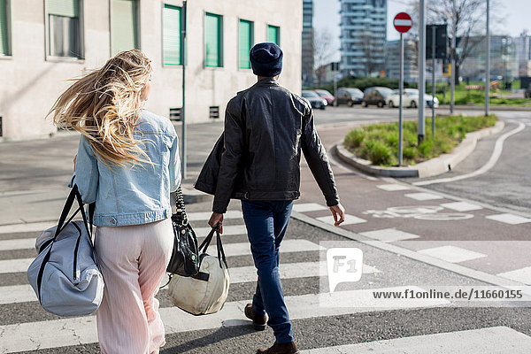 Young man and woman  crossing road carrying holdalls  rear view