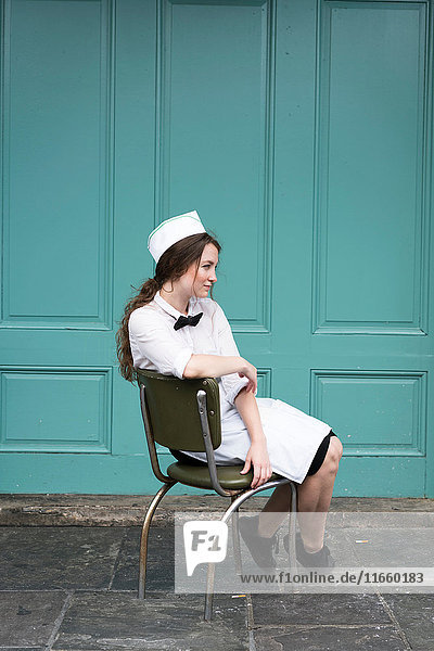 Frau in Kellnerinnen-Uniform auf Stuhl sitzend