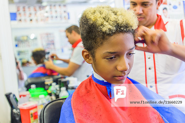 Hairdresser cutting teenage boy's hair in barbershop