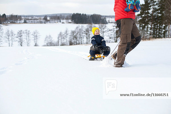 Vater zieht Sohn auf Schlitten mit  trägt Jungen auf dem Arm  in schneebedeckter Landschaft  niedriger Abschnitt