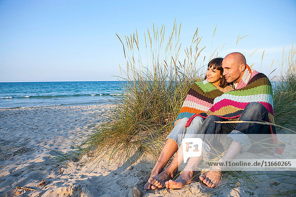 Couple covered with blanket on sand dune  Mallorca  Spain