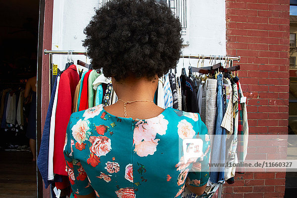 Rückansicht einer jungen weiblichen Mode-Bloggerin mit Afro-Haaren beim Betrachten einer Vintage-Kleiderstange  New York  USA