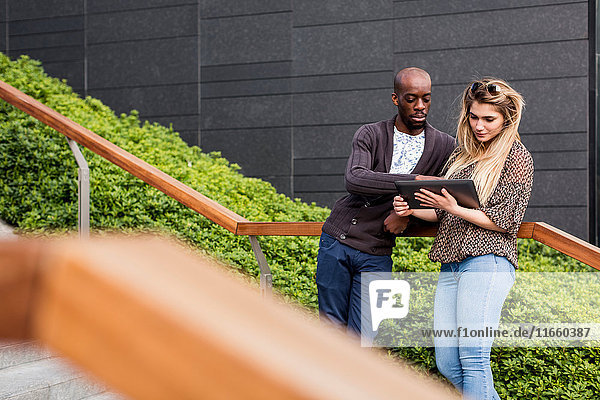 Ein junger Geschäftsmann und eine junge Frau  die ein digitales Tablett auf der Stadttreppe betrachten.