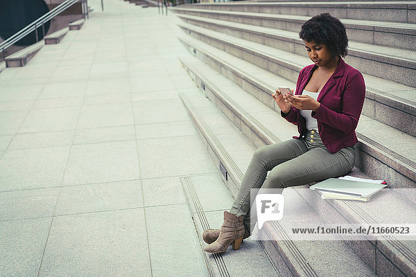Junge Frau sitzt auf einer Treppe und benutzt ein Smartphone