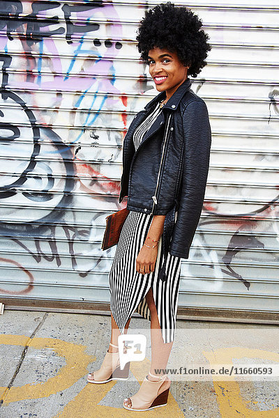 Stadtporträt einer jungen weiblichen Mode-Bloggerin mit Afro-Haaren an einer Graffiti-Wand  New York  USA