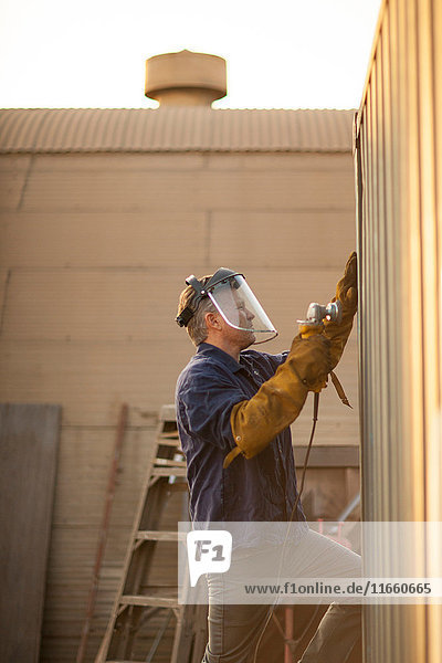 Welder using power tool on shipping container
