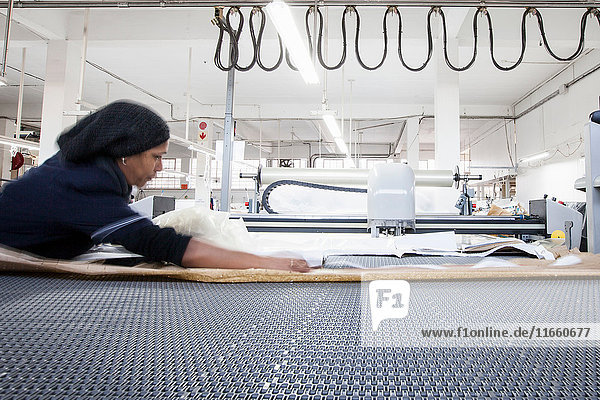 Fabrikarbeiterin  die in einer Bekleidungsfabrik Textilien für Maschinen vorbereitet