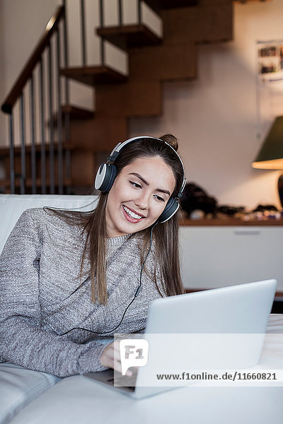 Junge Frau entspannt sich zu Hause  benutzt Laptop  trägt Kopfhörer