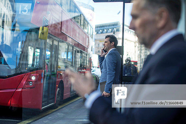 Geschäftsmann wartet an der Bushaltestelle mit Smartphone  London  UK