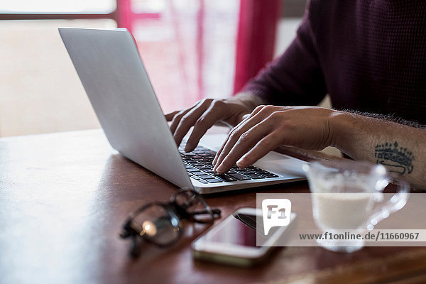 Young man sitting at table using laptop close-up mid section