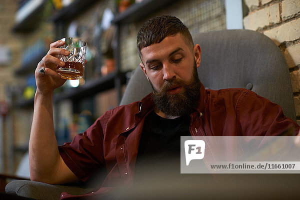 Young man with tumbler of spirit looking at menu in public house