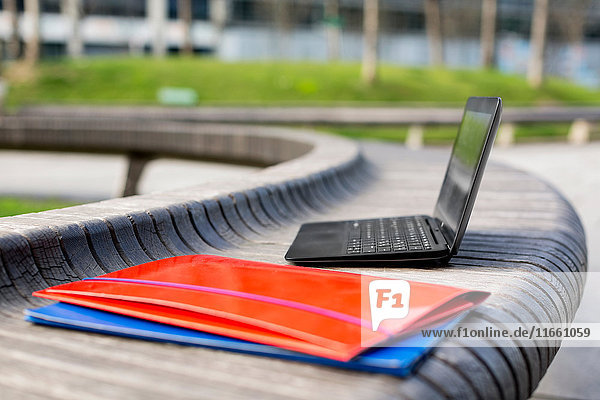 Open laptop and paperwork files on bench outdoors