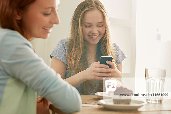 Mädchen im Cafe schaut auf Smartphone und lächelt