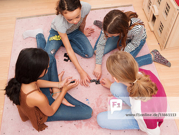Mädchen sitzen auf dem Boden und spielen Domino