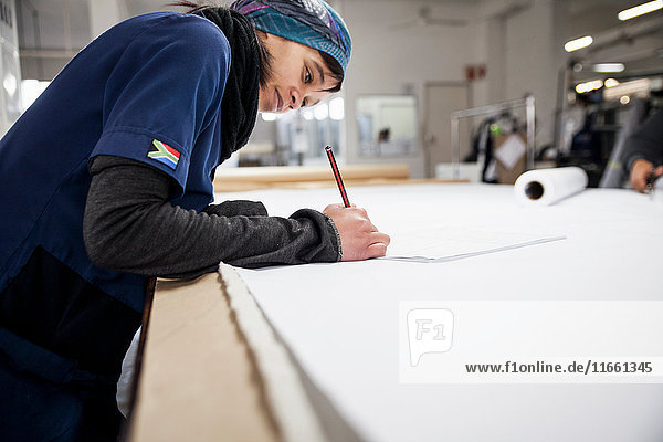 Fabrikarbeiter macht Notizen am Arbeitstisch in einer Bekleidungsfabrik
