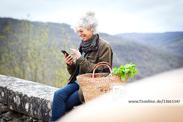 Frau sitzt an der Wand und schreibt SMS auf Smartphone  Bruniquel  Frankreich