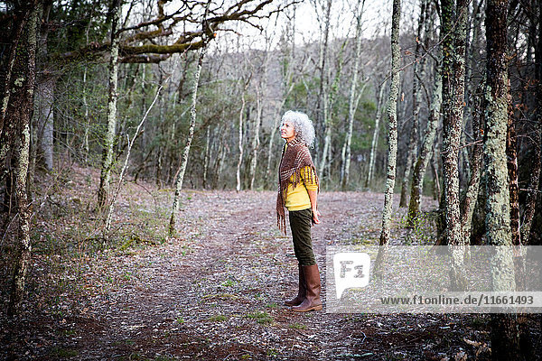 Reife Frau steht im Wald und schaut