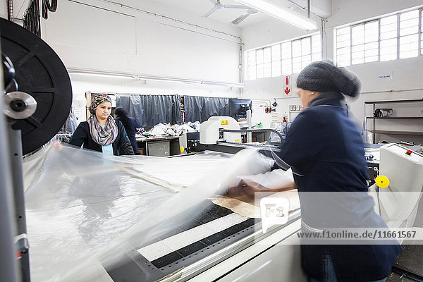 Fabrikarbeiterinnen rollen Textilien auf Musterschneidemaschine in Bekleidungsfabrik ab