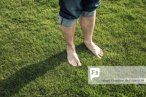 Beine und nackte Füße eines auf grünem Gras stehenden Mannes
