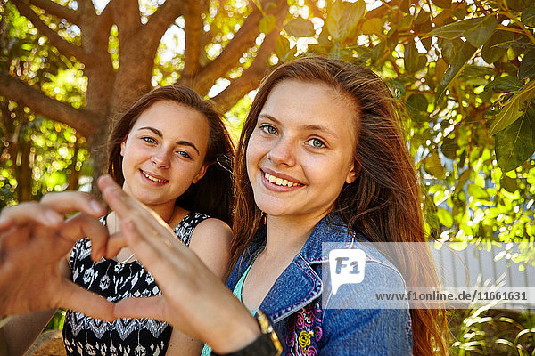 Portrait of two female friends in rural setting  making heart shape with hands