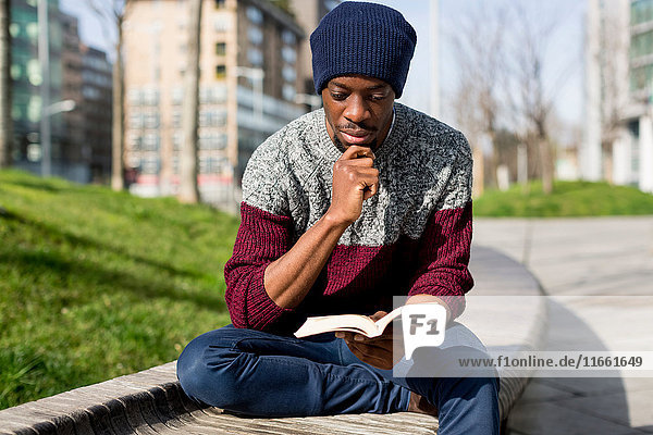 Mann sitzt auf Bank  liest Buch  nachdenklicher Ausdruck