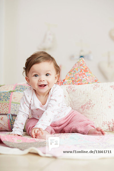 Porträt eines kleinen Mädchens,  das auf einer Decke sitzt und lacht