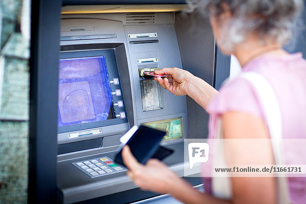 Reife Frau  die eine Kreditkarte in einen lokalen französischen Geldautomaten einführt